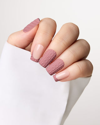 A close-up of a hand showcasing a manicure with alternating matte dusty rose textured nail wraps and smooth nude pink nail tips, set against a clean white background.